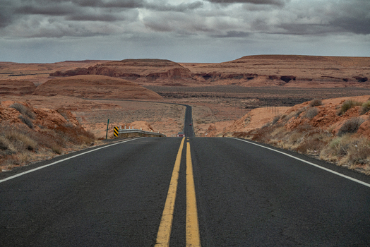 View of Monument Valley Tribal Park with a long asphalt road stretching through the desert landscape under a cloudy sky in Oljato Monument Valley Utah United States.