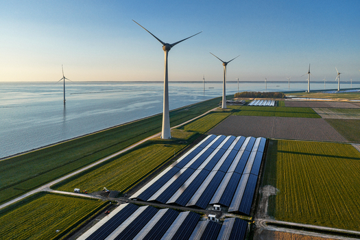 Aerial view of wind turbines and solar panels on a coastal farm with green fields and calm water under a clear sky Netherlands.