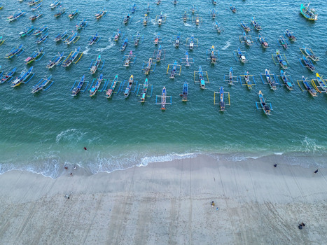 Aerial view of Papuma Beach with numerous colorful traditional fishing boats anchored in the turquoise sea along the sandy coastline in Jember East Java Indonesia. Aerial view of Papuma Beach with numerous colorful traditional fishing boats anchored in the turquoise sea along the sandy coastline in Jember East Java Indonesia.