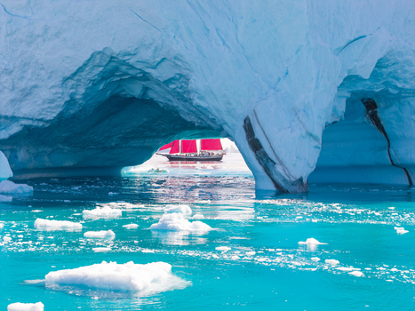 Aerial view of a red sailed ship framed by a natural ice arch in the turquoise Arctic waters of Greenland. Aerial view of a red sailed ship framed by a natural ice arch in the turquoise Arctic waters of Greenland.