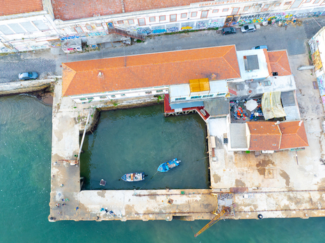 Aerial view of Ginjal Pier featuring historic buildings with orange roofs graffiti covered walls and small boats moored in the basin Almada Setubal Portugal. Aerial view of Ginjal Pier featuring historic buildings with orange roofs graffiti covered walls and small boats moored in the basin Almada Setubal Portugal.