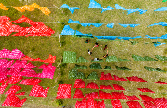 Narayanganj Bangladesh 30 March 2026 Aerial view of colorful fabrics laid out on the vibrant green grass as a group of people stand in a circle.