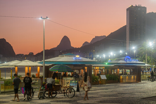 Rio de Janeiro Brazil 08 June 2026 View of Copacabana beach promenade at dusk with kiosks people walking on the mosaic sidewalk and the silhouette of Sugarloaf Mountain.