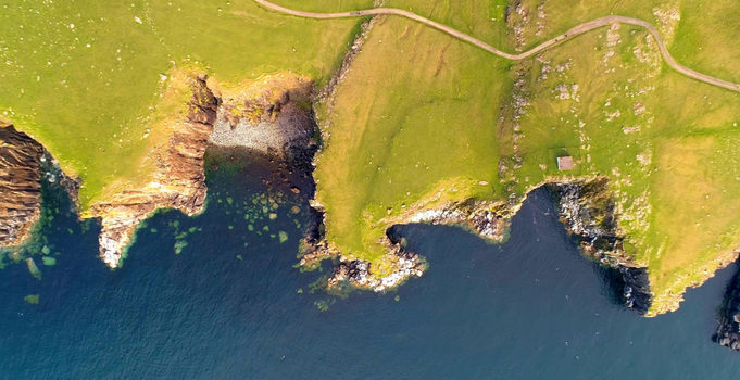 Aerial view of Duncansby Head Lighthouse situated on the rugged green cliffs overlooking the deep blue sea in Wick Scotland United Kingdom. Aerial view of Duncansby Head Lighthouse situated on the rugged green cliffs overlooking the deep blue sea in Wick Scotland United Kingdom.