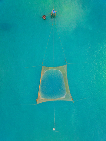 Aerial view of a traditional fishing net submerged in clear turquoise water with a small basket boat nearby in Vietnam. Aerial view of a traditional fishing net submerged in clear turquoise water with a small basket boat nearby in Vietnam.