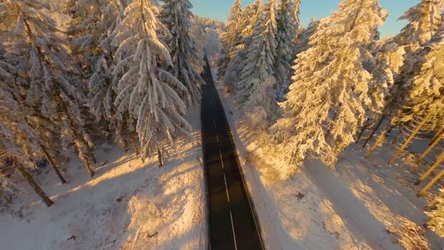 FPV aerial view of road through snowy forest Germany.