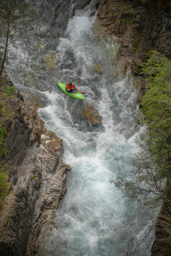 View of a kayaker in a green boat navigating the white water rapids of the Rio Manso canyon surrounded by steep rocky walls San Carlos de Bariloche Rio Negro Argentina. View of a kayaker in a green boat navigating the white water rapids of the Rio Manso canyon surrounded by steep rocky walls San Carlos de Bariloche Rio Negro Argentina.