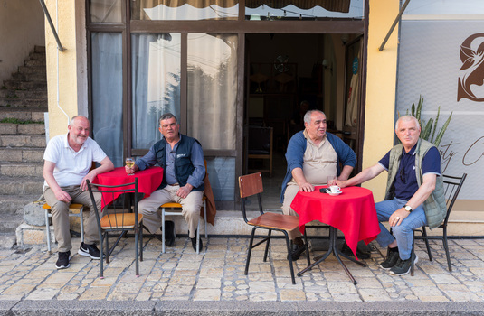Kruje Albania 12 June 2026 View of four men sitting at small tables with red tablecloths outside a cafe on a stone paved street in the historic town.
