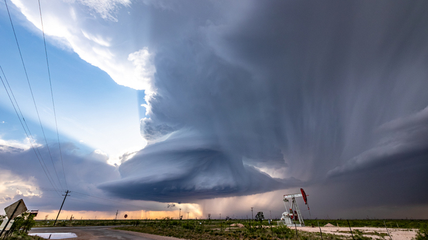 View of a dramatic supercell storm with dark swirling clouds and rain shafts over a rural landscape featuring an oil pump jack and power lines in Oklahoma City Oklahoma United States.