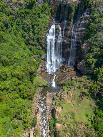 Aerial view of Bomburu Ella Waterfall cascading down rocky cliffs surrounded by lush green forest and flowing into a pool in Nuwara Eliya Central Province Sri Lanka. Aerial view of Bomburu Ella Waterfall cascading down rocky cliffs surrounded by lush green forest and flowing into a pool in Nuwara Eliya Central Province Sri Lanka.