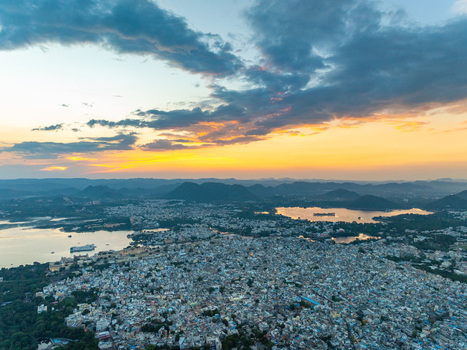 Aerial view of Udaipur with its dense urban layout historic buildings and Lake Pichola reflecting the golden sunset light in Udaipur Rajasthan India.