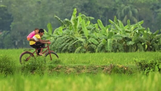 View of a boy riding a bicycle with a child on his back Bangladesh.