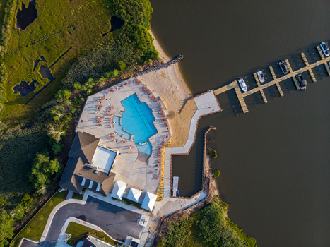 Ocean City Maryland United States 28 July 2019 Aerial view of a swimming pool and marina with boats docked at a pier surrounded by marshland and sandy shoreline.