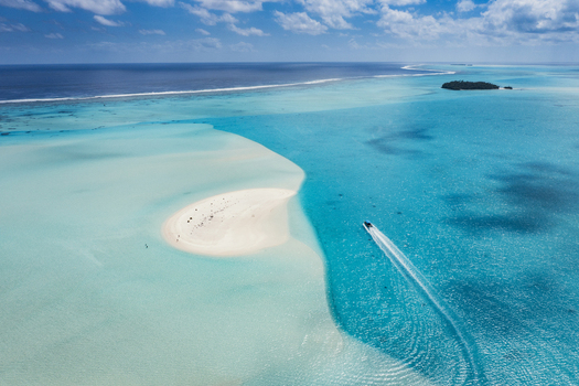 Aerial view of Aitutaki One Foot Island with its white sandbank surrounded by turquoise lagoon waters and a small boat leaving a wake in Arutanga Cook Islands. Aerial view of Aitutaki One Foot Island with its white sandbank surrounded by turquoise lagoon waters and a small boat leaving a wake in Arutanga Cook Islands.