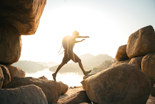 View of a hiker with a backpack jumping between large granite boulders during golden hour in the rocky landscape of Hampi Karnataka India. View of a hiker with a backpack jumping between large granite boulders during golden hour in the rocky landscape of Hampi Karnataka India.