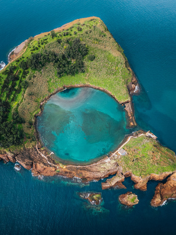 Aerial view of the vibrant turquoise waters fill the crater lake of Vila Franca do Campo ringed by lush green vegetation Sao Miguel Island Portugal.