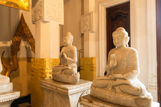 View of serene white marble Buddha statues in meditative poses within a temple interior featuring ornate pillars and warm lighting in Kandy Central Province Sri Lanka. View of serene white marble Buddha statues in meditative poses within a temple interior featuring ornate pillars and warm lighting in Kandy Central Province Sri Lanka.