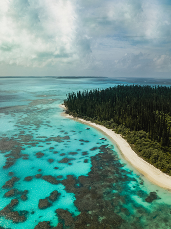 Aerial view of the vibrant turquoise waters meet the pristine white sands fringed by the lush green forest of Île des Pins Pine Island New Caledonia. Aerial view of the vibrant turquoise waters meet the pristine white sands fringed by the lush green forest of Île des Pins Pine Island New Caledonia.