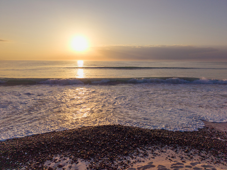 Aerial view of the sun kissing the tranquil sea its golden light reflecting on the gentle waves and dark rocks Kadrihnitin Socotra Yemen. Aerial view of the sun kissing the tranquil sea its golden light reflecting on the gentle waves and dark rocks Kadrihnitin Socotra Yemen.