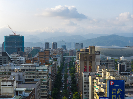 Aerial view of the Taipei city skyline featuring the Taipei Dome dense urban residential buildings construction cranes and distant mountains under a cloudy sky in Taipei Taiwan. Aerial view of the Taipei city skyline featuring the Taipei Dome dense urban residential buildings construction cranes and distant mountains under a cloudy sky in Taipei Taiwan.