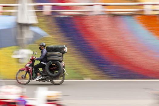 Hanoi Vietnam 11 November 2025 View of a motorcyclist carrying a large stack of tires past a vibrant colorful mural.