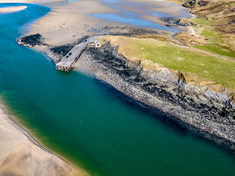Aerial view of Ballyness Bay featuring a stone pier extending into turquoise water surrounded by sandy tidal flats and green coastal fields in Ballyness County Donegal Ireland. Aerial view of Ballyness Bay featuring a stone pier extending into turquoise water surrounded by sandy tidal flats and green coastal fields in Ballyness County Donegal Ireland.