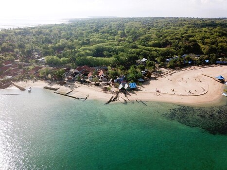 Aerial view of a coastal village with traditional houses sandy beach and lush tropical trees bordering the turquoise sea in Sumenep East Java Indonesia.