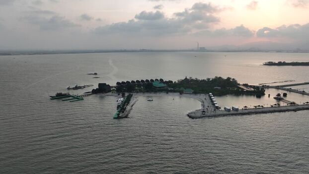 Aerial view of Pulau Lima Resort featuring a small island with lush greenery wooden structures a pier and calm waters at sunset in Kasemen Banten Indonesia. Aerial view of Pulau Lima Resort featuring a small island with lush greenery wooden structures a pier and calm waters at sunset in Kasemen Banten Indonesia.