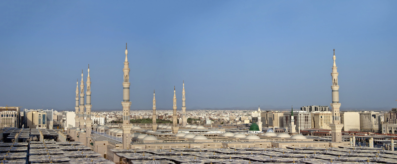 View of Al Masjid e Nabawi with its iconic minarets green dome and extensive courtyard umbrellas under a clear blue sky in Madinah Al Madinah Province Saudi Arabia.