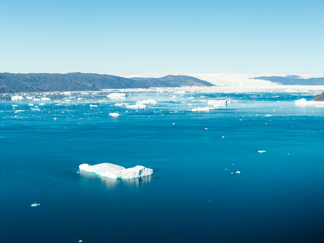 Aerial view of icebergs floating in the deep blue sea with distant snow capped mountains and a clear sky in Greenland. Aerial view of icebergs floating in the deep blue sea with distant snow capped mountains and a clear sky in Greenland.