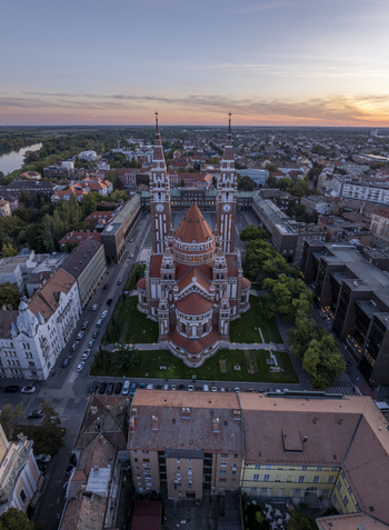 Aerial view of the iconic Szeged Cathedral surrounded by historic rooftops and urban streets under a soft sunset sky in Szeged Hungary. Aerial view of the iconic Szeged Cathedral surrounded by historic rooftops and urban streets under a soft sunset sky in Szeged Hungary.