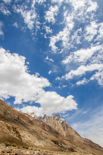 View of the rugged mountain peaks near K2 Base Camp with rocky slopes and a bright blue sky with scattered white clouds in Ghakhar Gilgit Pakistan. View of the rugged mountain peaks near K2 Base Camp with rocky slopes and a bright blue sky with scattered white clouds in Ghakhar Gilgit Pakistan.
