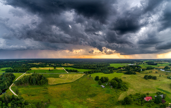 Aerial view of dramatic storm clouds over a lush green rural landscape with fields forests and scattered houses at sunset Latvia. Aerial view of dramatic storm clouds over a lush green rural landscape with fields forests and scattered houses at sunset Latvia.