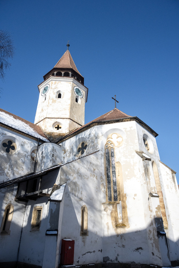 View of the historic Prejmer Fortified Church with its tall bell tower gothic windows and white stone walls under a clear blue winter sky in Prejmer Brasov Romania. View of the historic Prejmer Fortified Church with its tall bell tower gothic windows and white stone walls under a clear blue winter sky in Prejmer Brasov Romania.