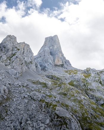 View of a jagged rocky mountain peak piercing the sky amidst a sea of grey stone and sparse green vegetation Picos de Europa Asturias Spain. View of a jagged rocky mountain peak piercing the sky amidst a sea of grey stone and sparse green vegetation Picos de Europa Asturias Spain.