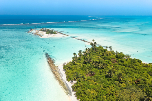 Aerial view of a lush tropical island with tall palm trees and dense vegetation surrounded by crystal clear turquoise lagoon water Innafinolhu Haa Alif Atoll Maldives. Aerial view of a lush tropical island with tall palm trees and dense vegetation surrounded by crystal clear turquoise lagoon water Innafinolhu Haa Alif Atoll Maldives.