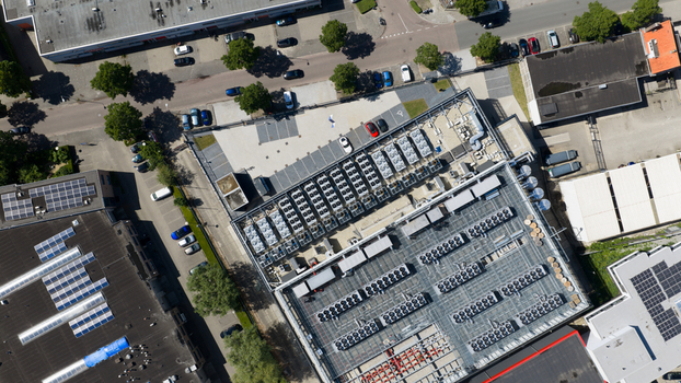 Aerial view of Switch Datacenters AMS4 with rows of cooling units on the roof and solar panels on adjacent buildings in Diemen Noord Holland Netherlands. Aerial view of Switch Datacenters AMS4 with rows of cooling units on the roof and solar panels on adjacent buildings in Diemen Noord Holland Netherlands.