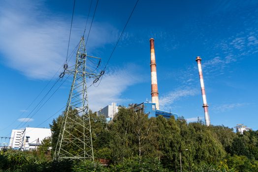 View of a power plant with tall chimneys and a power transmission tower set against a clear blue sky in Poland.