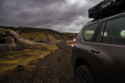 View of a car parked on a rugged gravel road amidst a landscape of moss covered lava fields under a dramatic overcast sky Skaftárhreppur Iceland. View of a car parked on a rugged gravel road amidst a landscape of moss covered lava fields under a dramatic overcast sky Skaftárhreppur Iceland.
