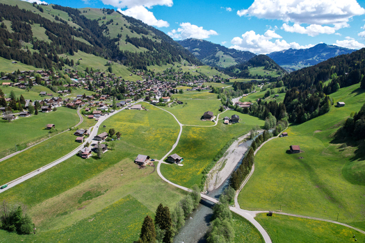 Aerial view of Rougemont with traditional chalets lush green meadows a winding river and forested mountains Rougemont Vaud Switzerland. Aerial view of Rougemont with traditional chalets lush green meadows a winding river and forested mountains Rougemont Vaud Switzerland.