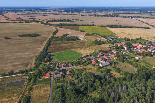 Aerial view of the rural village of Grimme surrounded by vast agricultural fields scattered trees and distant wind turbines in Bruessow Brandenburg Germany. Aerial view of the rural village of Grimme surrounded by vast agricultural fields scattered trees and distant wind turbines in Bruessow Brandenburg Germany.