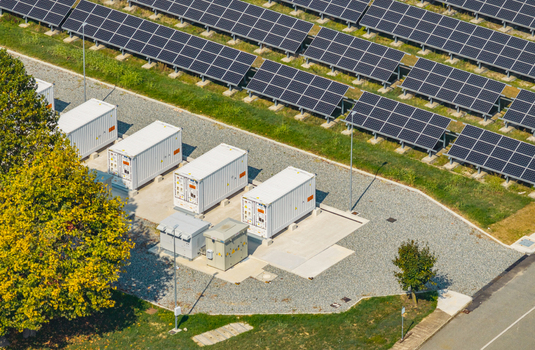 Aerial view of grid scale battery storage containers beside a large solar farm showcasing renewable energy integration and modern electricity infrastructure in Italy.