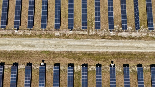 Aerial view of rows of solar panels contrast sharply against the dry grassy landscape divided by a pale dirt path Elkton Florida United States. Aerial view of rows of solar panels contrast sharply against the dry grassy landscape divided by a pale dirt path Elkton Florida United States.