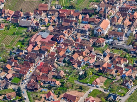 Aerial view of terracotta rooftops nestled amongst verdant trees the church steeple piercing the skyline casting shadows over the quaint village Kintzheim Grand Est France.