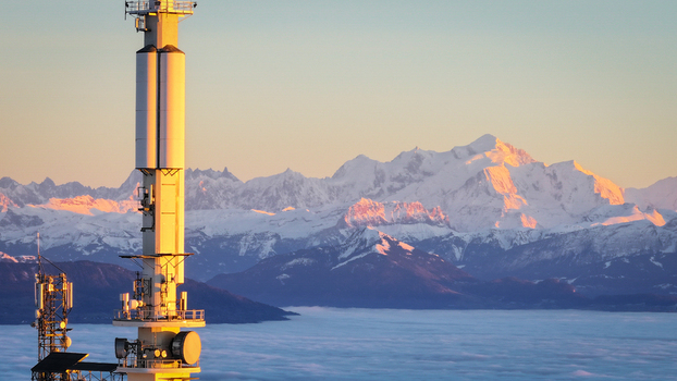 Aerial view of the Mont Blanc massif and a telecommunications tower rising above a sea of clouds during golden hour in Chamonix Auvergne Rhone Alpes France. Aerial view of the Mont Blanc massif and a telecommunications tower rising above a sea of clouds during golden hour in Chamonix Auvergne Rhone Alpes France.