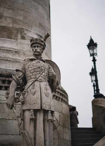 View of a stone soldier statue stands guard its weathered face and ornate uniform a stark contrast to the smooth column behind Budapest Hungary. View of a stone soldier statue stands guard its weathered face and ornate uniform a stark contrast to the smooth column behind Budapest Hungary.