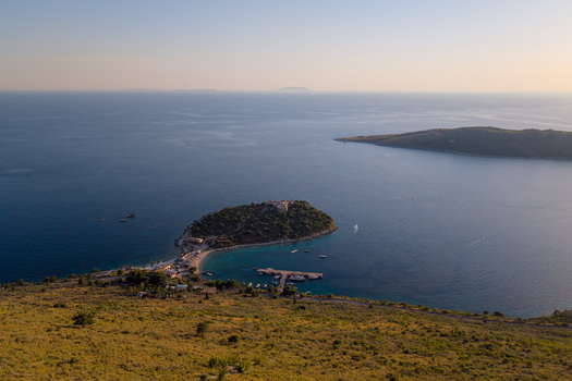 Aerial view of Porto Palermo Castle on a green peninsula surrounded by the blue waters of the Ionian Sea with boats in the harbor Porto Palermo Qarku i Vlores Albania. Aerial view of Porto Palermo Castle on a green peninsula surrounded by the blue waters of the Ionian Sea with boats in the harbor Porto Palermo Qarku i Vlores Albania.