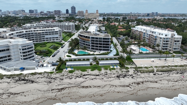 Aerial view of pristine white buildings lining the beach contrasting with the deep blue pools and the distant city skyline Palm Beach Florida United States.