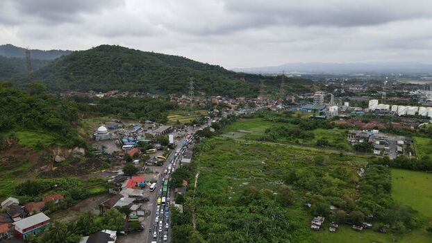 Aerial view of the Merak area featuring a busy road with traffic lush green hills industrial facilities and residential buildings in Pulomerak Banten Indonesia. Aerial view of the Merak area featuring a busy road with traffic lush green hills industrial facilities and residential buildings in Pulomerak Banten Indonesia.