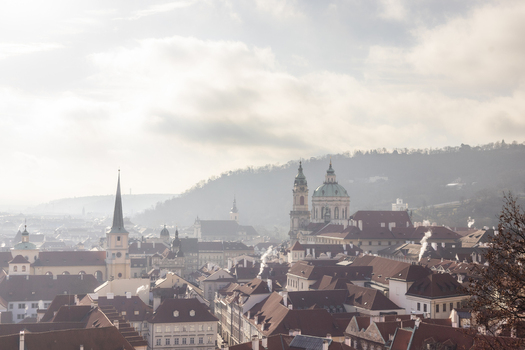 View of the historic red rooftops of Mala Strana with St. Nicholas Church and Petrin Hill under a soft morning mist in Prague Prague Czechia. View of the historic red rooftops of Mala Strana with St. Nicholas Church and Petrin Hill under a soft morning mist in Prague Prague Czechia.